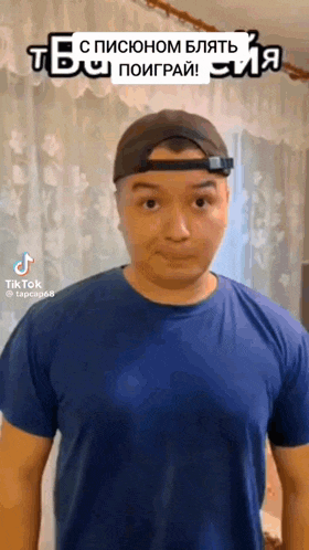 a man wearing a hat and a blue shirt is standing in front of a curtain .