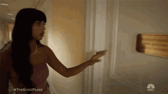 a woman is standing in a hallway pointing at a sign on the wall .