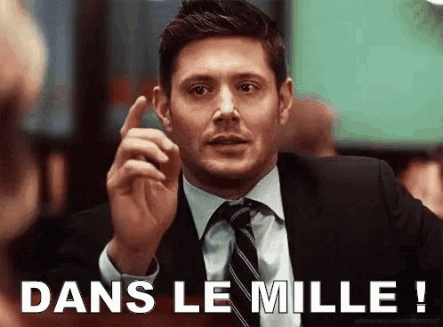 a man in a suit and tie is pointing his finger at the camera and says dans le mille !