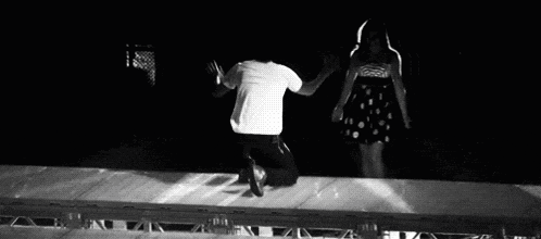 a black and white photo of a man kneeling down next to a woman on a stage .