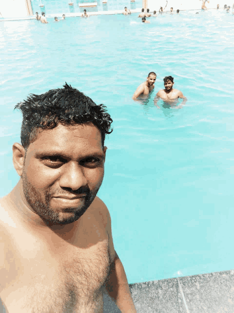 a shirtless man takes a selfie in a pool