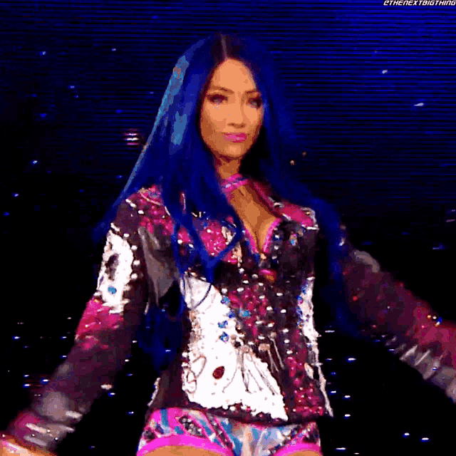 a woman with blue hair is standing on a stage wearing a pink and black outfit .