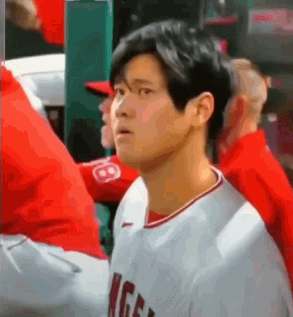 a baseball player is standing in the dugout and looking at the camera with a surprised look on his face .