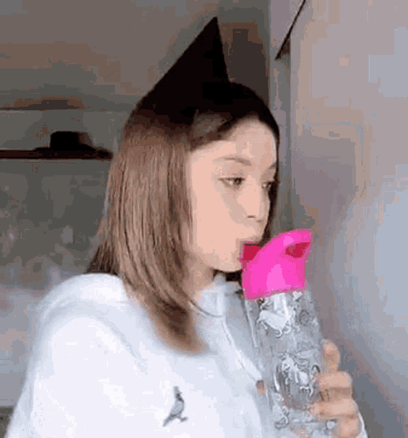 a young girl is drinking water from a pink water bottle .