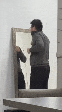 a man is looking at himself in a mirror while holding a cup .