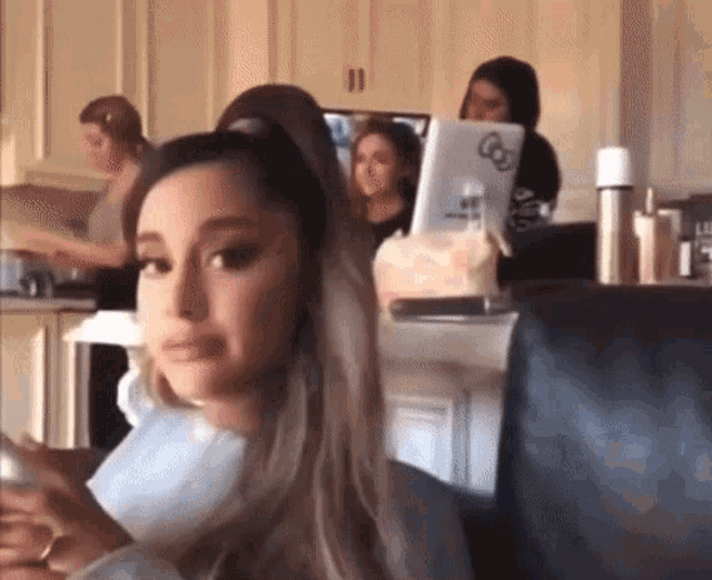 ariana grande is sitting in a chair with a laptop on her lap and looking at her phone .