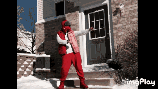 a man in a red vest is standing in front of a brick house with the word imgplay on the bottom