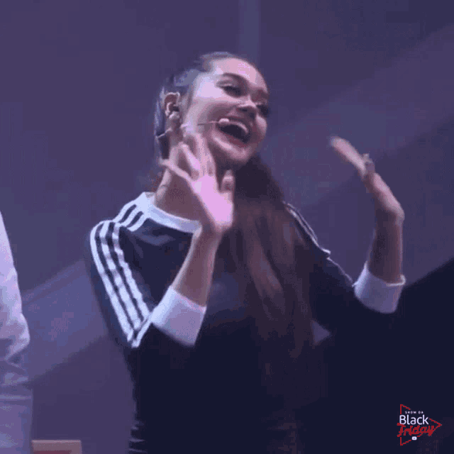 a woman in a black and white adidas shirt is waving