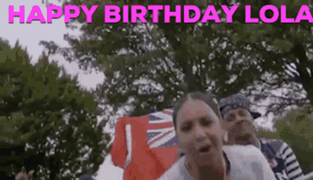 a woman is standing in front of a crowd holding a british flag and a sign that says `` happy birthday lola '' .