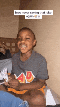 a young boy wearing a shirt that says ad is sitting on a bed