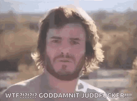 a man with a beard and long hair is standing in a field with a serious look on his face .