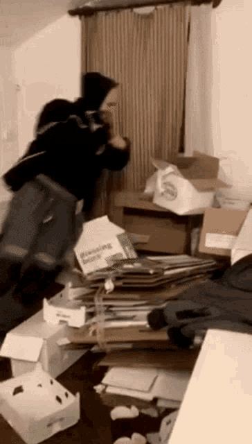 a person is jumping in the air in a room filled with boxes and a pizza box .