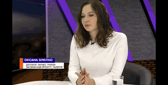 a woman is sitting at a table with a glass of water in front of her and the name oksana is on the screen