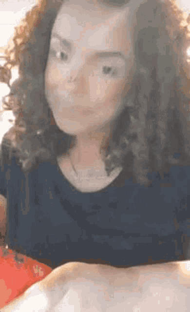 a woman with curly hair is wearing a black shirt and necklace .