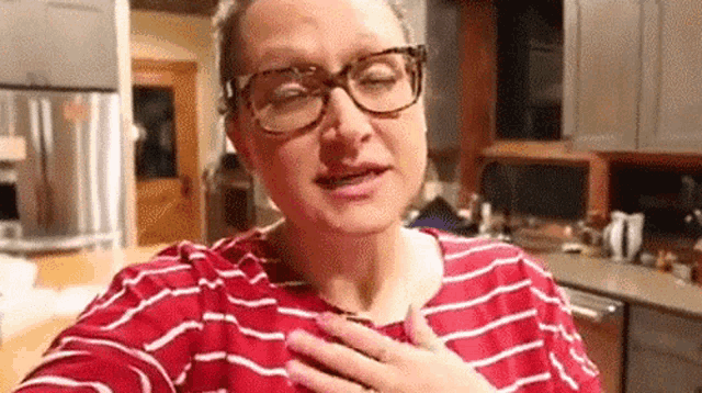 a woman wearing glasses and a red and white striped shirt is taking a selfie in the kitchen .