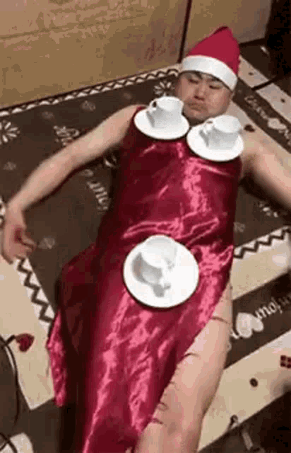 a man in a santa hat is laying on a bed with cups and saucers on his shoulder .