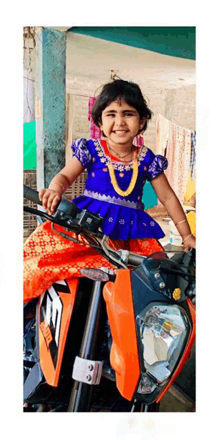 a little girl in a blue dress is sitting on a motorcycle .