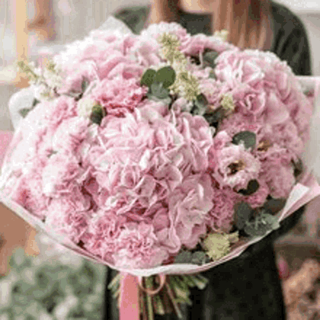 a woman is holding a bouquet of pink flowers wrapped in pink paper .