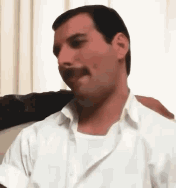 a man with a mustache is wearing a white shirt and sitting on a chair .