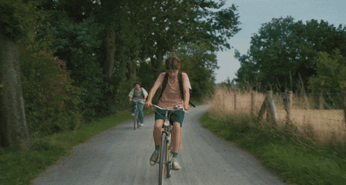 a boy and a girl are riding bikes down a country road
