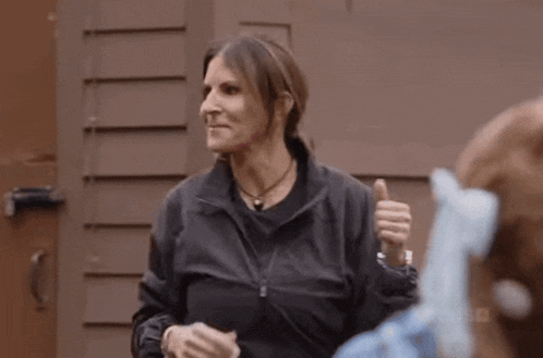 a woman in a black jacket is giving a thumbs up in front of a building .