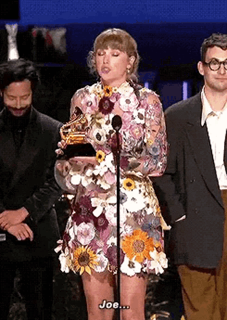 a woman in a floral dress is standing on a stage holding a microphone .