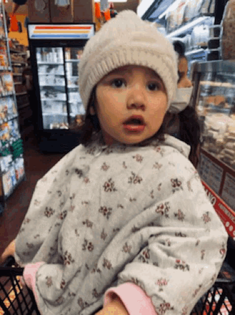 a little girl wearing a white hat is sitting in a grocery cart