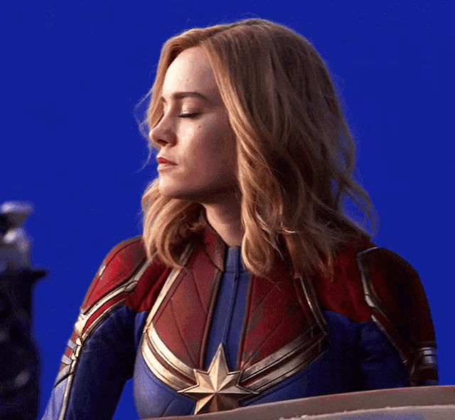 a woman in a captain marvel costume is standing in front of a blue screen .