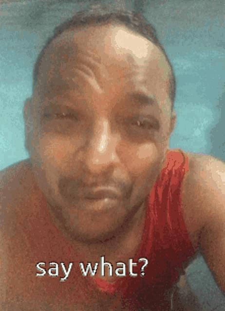 a man is wearing a red tank top and says say what