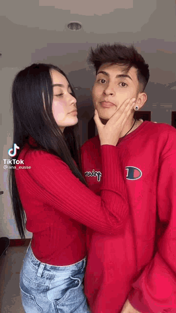 a woman in a red shirt is touching a man 's face with her hand