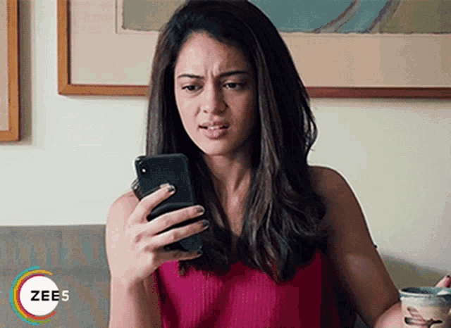 a woman is sitting on a couch looking at her cell phone with a zees logo in the corner