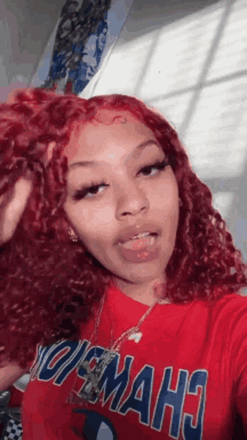 a girl with red curly hair is taking a selfie with her tongue out .