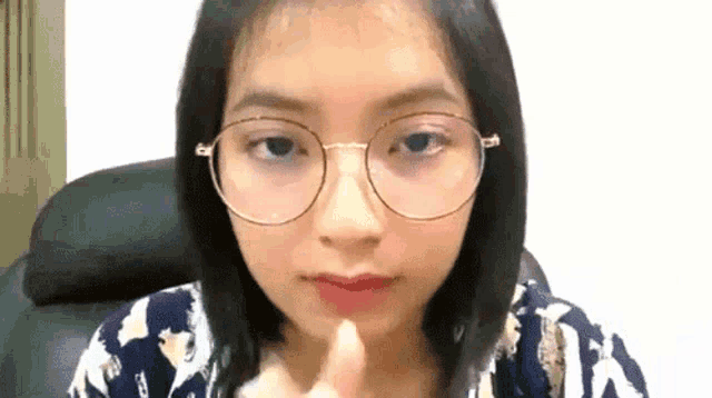 a young woman wearing glasses is sitting in a chair and making a funny face .