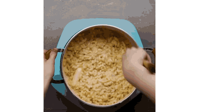 a person stirring a pot of macaroni and cheese with a wooden spoon .