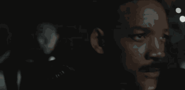 a close up of a man 's face in a dark room with a police officer in the background .