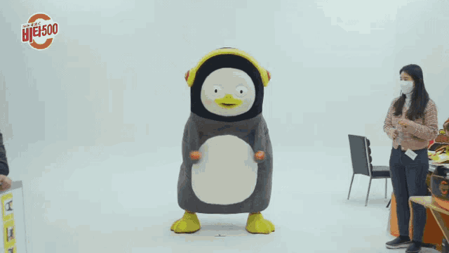a woman wearing a face mask stands next to a stuffed penguin with the number 500 on it