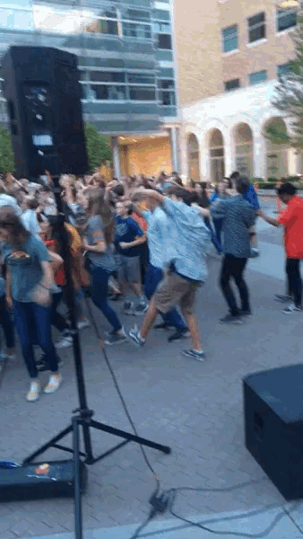 a large group of people are dancing in front of a speaker