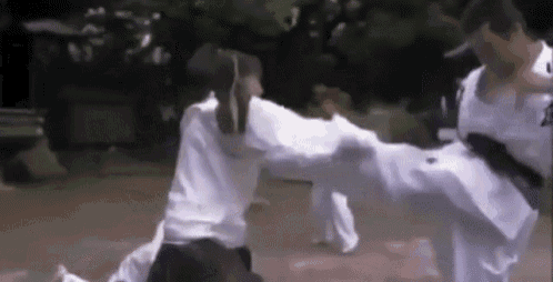 a man is kicking another man in the face while a woman watches .