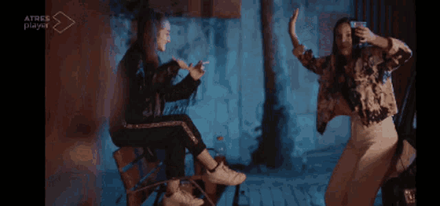 a woman sitting on a chair smoking a cigarette and another woman dancing in front of a sign that says atres player