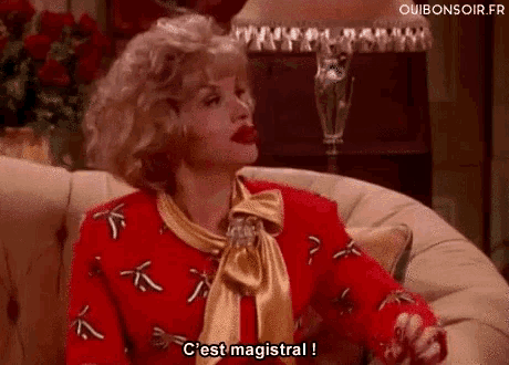 a woman in a red sweater and gold scarf is sitting on a couch and saying c'est magistral .