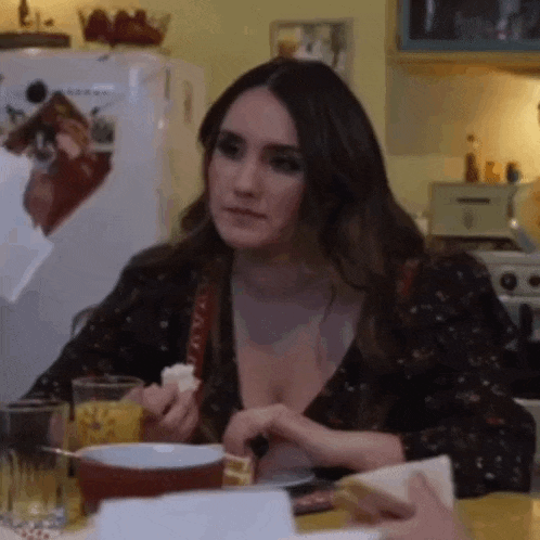 a woman is sitting at a table in a kitchen eating a sandwich .