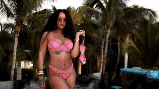 a woman in a pink bikini is standing by a pool holding a pink bra .