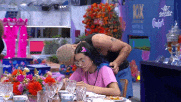 a man and a woman are sitting at a table with a 10x sign in the background