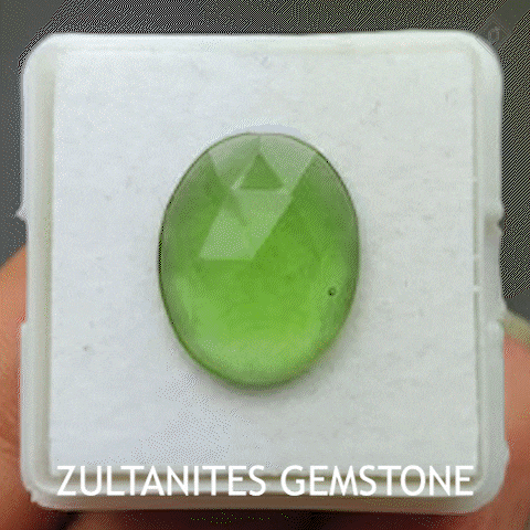 a person is holding a green stone in a display case that says zultanite gemstone