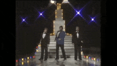 three men in tuxedos are dancing on a stage in a dark room .
