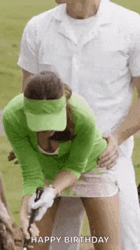 a woman in a green shirt is holding a golf club while a man holds her waist .