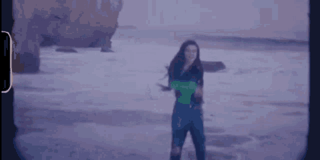 a woman in a green sweater is dancing on a beach .