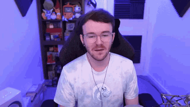 a man with glasses and headphones is sitting in a chair in front of a microphone .