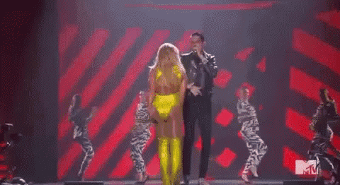 a man is singing into a microphone on a stage while a woman is dancing .