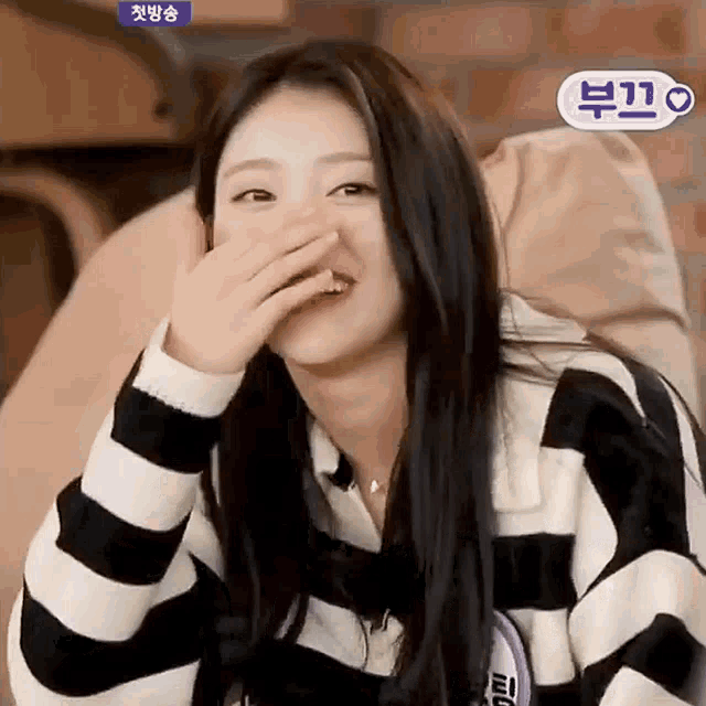 a woman in a striped sweater is covering her mouth with her hand while sitting on a bean bag chair .